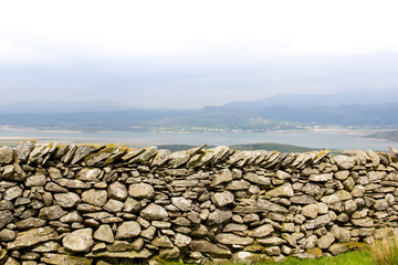 Mastery of craft, a brilliantly built stone wall with a beach and town in the distance behind. 