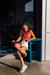 Stylish happy young brunette woman wearing white shorts and sneakers holding pink cup of coffee to go.