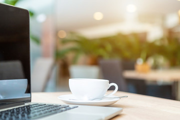 Close-up of Business laptop computer and coffee cup on wooden table of In the coffee shop background