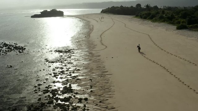 Drone shot of a child bareback riding a horse on a sandy beach, Sumba, with the ocean in the background