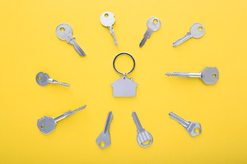 Keys and trinket in shape of house in the center on color background, top view.