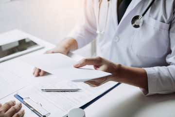 Asian male doctor talking in clinic room and handing a prescription to the patient.