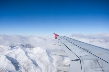 Aerial view of Himalayas mountain range, cloud blue sky and plane wing view through the airplane window.