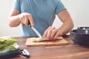 A person cuts fresh white asparagus into small pieces. The board was photographed on the cut with the hands of the person