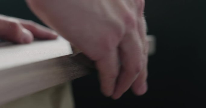 Slow motion woodworker hand sanding walnut board with sand block