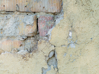 Old weathered brick wall fragment with cracked yellow stucco