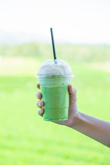 Fresh matcha green tea frappe drink beverage with blur  plantation farm background.