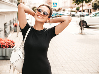 Portrait of beautiful smiling hipster model dressed in summer clothes. Trendy girl posing in the street background in sunglasses. Funny and positive woman having fun