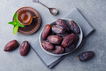Fresh Medjool Dates in a bowl with tea. Ramadan kareem. Grey stone background. Top view.