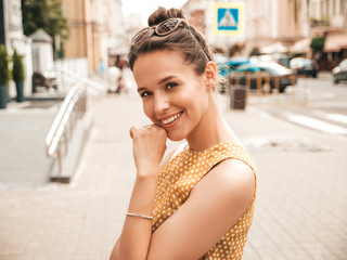 Portrait of beautiful smiling hipster model dressed in summer yellow dress. Trendy girl posing in the street background. Funny and positive woman having fun