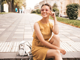 Portrait of beautiful smiling hipster model dressed in summer yellow dress. Trendy girl posing in...