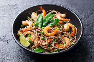 Stir fry noodles with vegetables and shrimps in black bowl. Slate background. Close up.