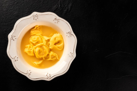 Italian Tortellini In Broth, Overhead Shot On A Black Background With Copyspace