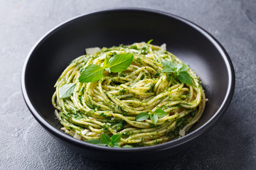 Pasta spaghetti with pesto sauce in black bowl. Grey background. Close up.