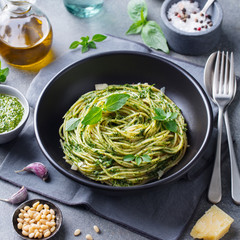 Pasta spaghetti with pesto sauce and fresh basil leaves in black bowl. Grey background.