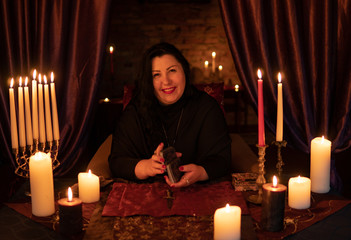 Fortune teller woman in dark room with lots of candles guesses on a tarot card deck