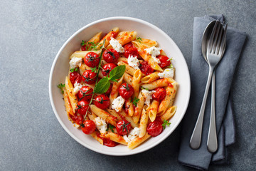 Pasta penne with roasted tomato, sauce, mozzarella cheese. Grey stone background. Top view.