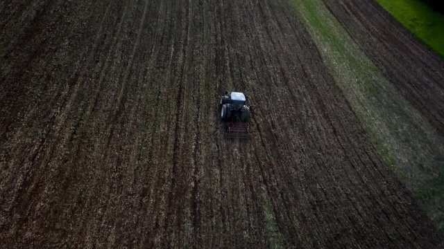 scenic 4K aerial footage of the farming tractor plowing the field in an urban environment at sunset. cinematographic stock video of the blue tractor ploughing the acre at sunset from birds view.