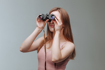 Girl looking through binoculars on a gray background