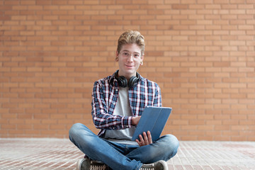 Cute young man looking at the camera while holding an a tablet with one hand.