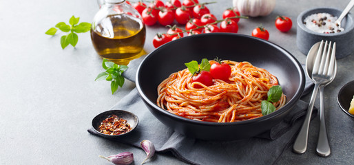 Pasta, spaghetti with tomato sauce in black bowl on grey background. Copy space.