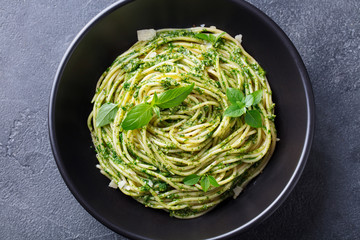 Pasta spaghetti with pesto sauce and fresh basil leaves in black bowl. Grey background. Close up. Top view.