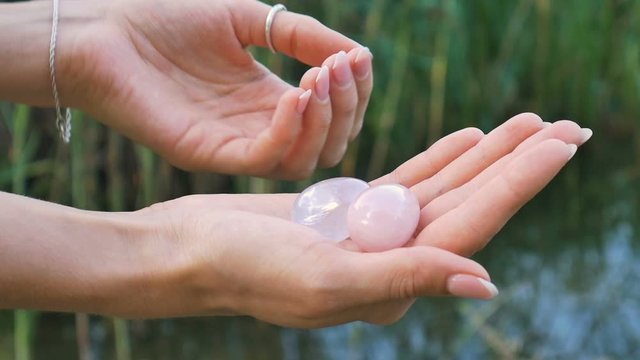 Female hand holding a rose quartz and amethyst crystal yoni eggs on river background. Women's health, unity with nature concepts