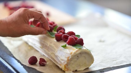 Hand decorating cake roll with raspberries, cake decorating