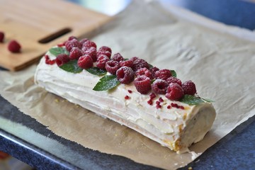 Cake roll with white cream decorated with raspberries and mint leaves