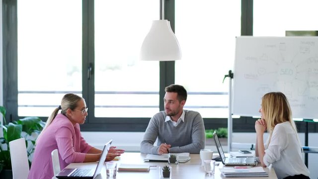 Woman and businessman talking while leaving the office. Behind, their partners continue to debate in the office.