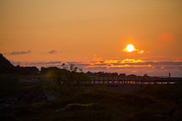 Photo of scenic area, houses, orange sky, bridge at sunset in Norway.
