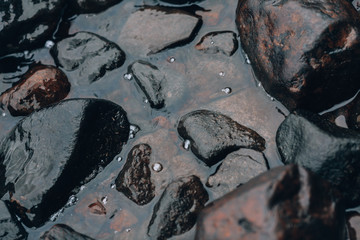 Stones in the water. Gloomy photo background with river stones. Cliffs covered with water, close-up