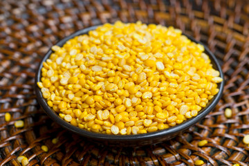 Yellow lentil in black bowl on wooden rattan tray. Close up.