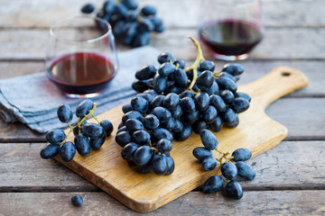 Glass of red wine with fresh grape on wooden table.