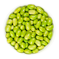Edamame. Green soybeans in white bowl. Mukimame, unripe soya beans outside the pod. Glycine max, a legume, edible after cooking and a protein source. Closeup, on white background, macro food photo.