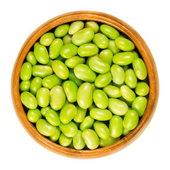Edamame. Green soybeans in wooden bowl. Mukimame, unripe soya beans outside the pod. Glycine max, a legume edible after cooking and a protein source. Closeup, on white background, macro food photo.