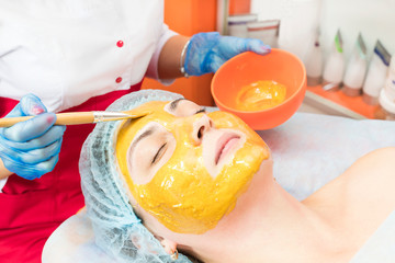 The procedure in the beauty salon applying a personal mask on the face of a woman with a mask of components of the ferrous and non-ferrous metals.
