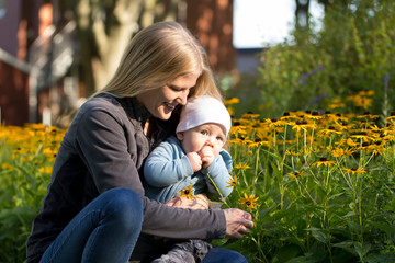 Fototapeta na wymiar Horizontal portrait of adorable baby boy in his pretty young mother’s arms tasting yellow coneflower during beautiful late summer afternoon