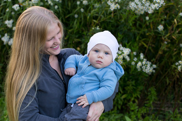 Medium horizontal portrait of pretty young blond mother holding adorable baby boy with solemn expression outdoors during late summer afternoon