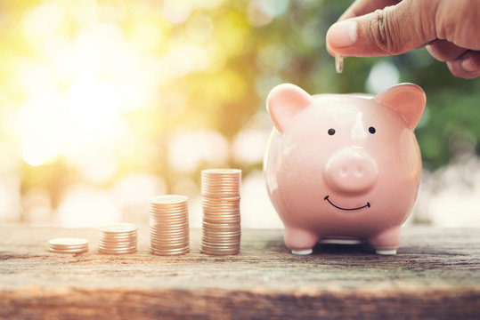 Woman Hands Hold Coins Putting Coin In Piggy Bank With Money Stack Step On Wood Table In The Public Park.money Saving Financial Concept.retro Vintage Color Tone.