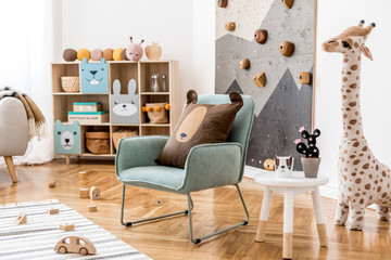 Modern scandinavian interior design of childroom with mint armchair, climbing wall for kids, design furnitures, soft toys, teddy bear and cute children's accessories. Stylish kidroom decor. Template.