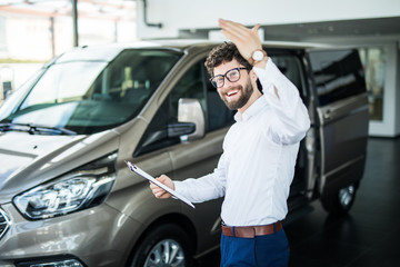 Handsome car dealership worker smiling while standing near the car