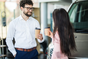 Dealer speaking with a client in a dealership while drinking coffee and discuss car purchase