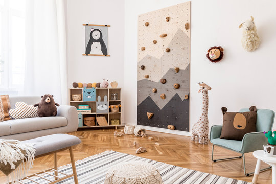 Stylish scandinavian interior design of childroom with gray sofa, modern climbing wall for kids, design furnitures, soft toys, teddy bear and cute children's accessories. Mock up poster. Template.