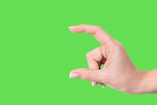 Closeup view of beautiful white manicured female hand showing size of virtual invisible object with help of two fingers isolated on green background. Horizontal color photography.