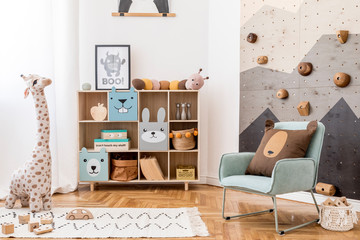 Scandinavian interior design of playroom with modern climbing wall for kids, design furnitures, mint armchair, soft toys, teddy bear and cute children's accessories. Mock up poster frame. Template.