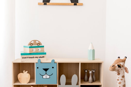 Stylish scandinavian child room with wooden cabinet, toys, boxes and plush teddy. White walls, Minimalistic home decor of playroom. Template. Copy space. 