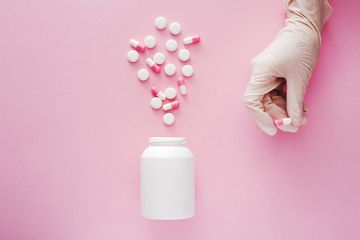 Different pills drugs or tablets spilling out of a white plastic medicine bottle. Female doctor hand with capsule. Health care concept. Top view with copy space.