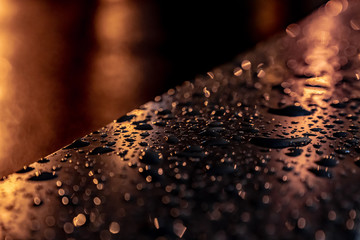 Metal surface at night with drops of rain. Night lights reflects on the surface. Dark image. Picture for wallpaper, text, design or any purpose. Narrow field of depth. Background is blurred