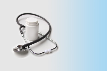 medical stethoscope lies on a light background around a white empty medicine can, form for a designer, close-up, copy space